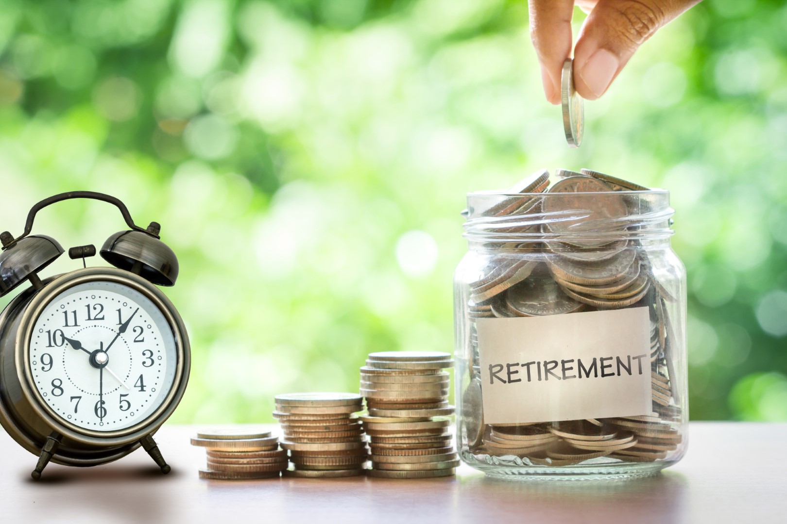 Hand putting Coins in glass jar with retro alarm clock for time